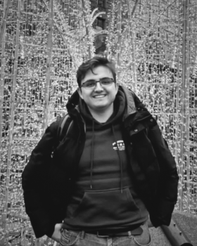 Auf dem schwarz-weiß Bild ist ein junger Mann mit Brille und Hoodie abgebildet, der in die Kamera lächelt.